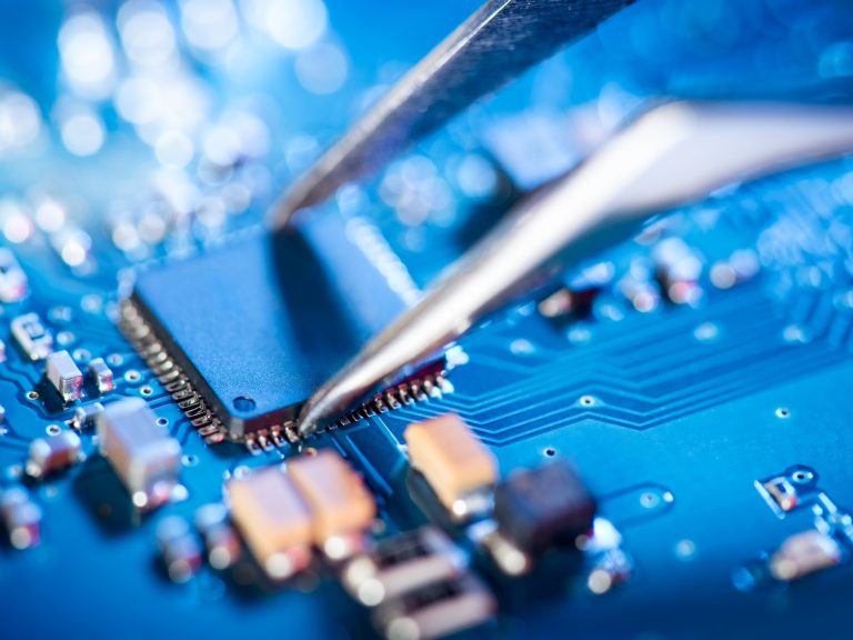 Componente eletrônico sendo posicionado com pinça numa placa de circuito